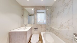 A modern bathroom with a marble wall, a large mirror, a sink, a toilet, and a bathtub.