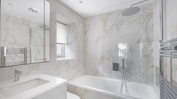 A modern bathroom with a marble shower, a large mirror, and a separate sink.