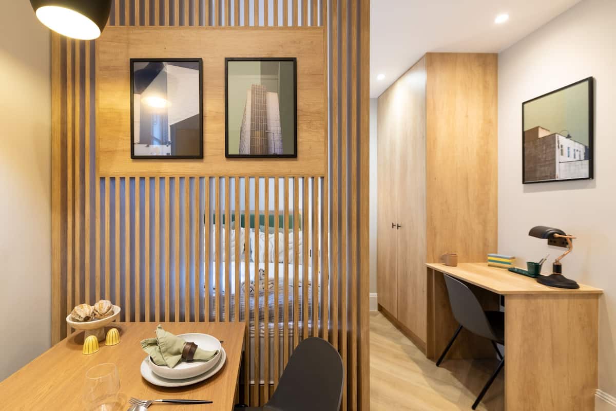 Une chambre d’hôtel moderne avec une cloison en bois, un coin repas comprenant une table et des chaises, un bureau avec une chaise, et deux tableaux encadrés accrochés au mur.