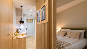 Una habitación de hotel moderna con un armario de madera, una cama con cabecero verde, una mesita de noche y un cuadro colgado en la pared.