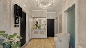 Un pasillo con piso de madera, un sillón blanco, una planta en maceta y una lámpara moderna.