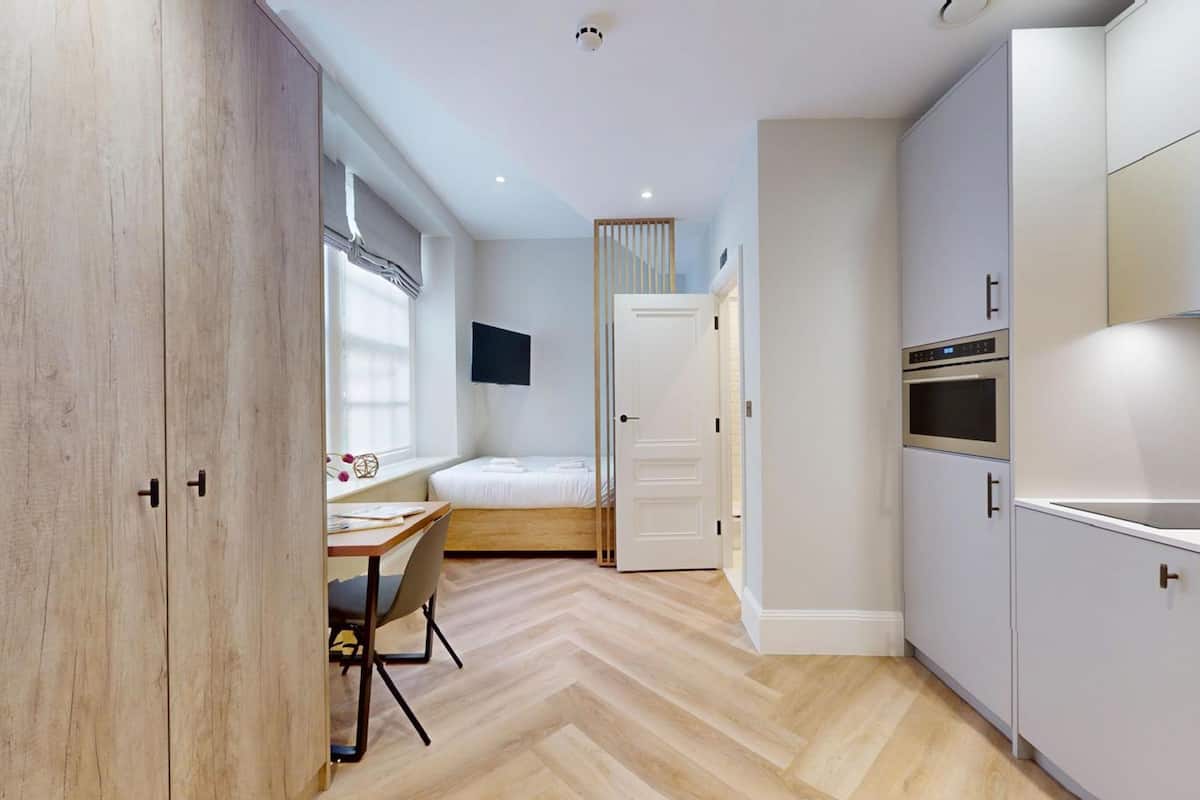 Une chambre compacte et moderne, équipée d’un lit, d’un bureau et d’une kitchenette.