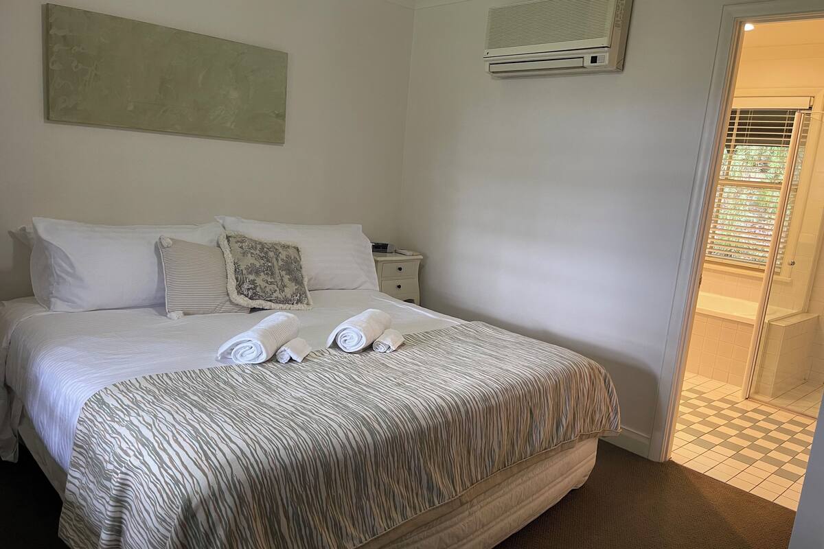 A neatly made bed with a striped bedspread, a pillow, and rolled towels on the bed.