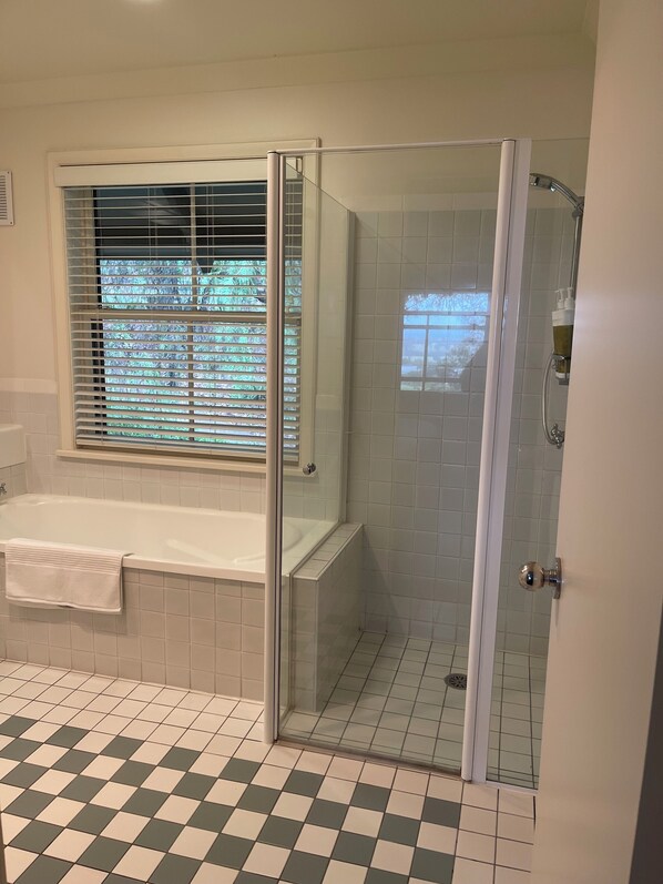 A bathroom with a bathtub, a shower enclosure, and a window with blinds.