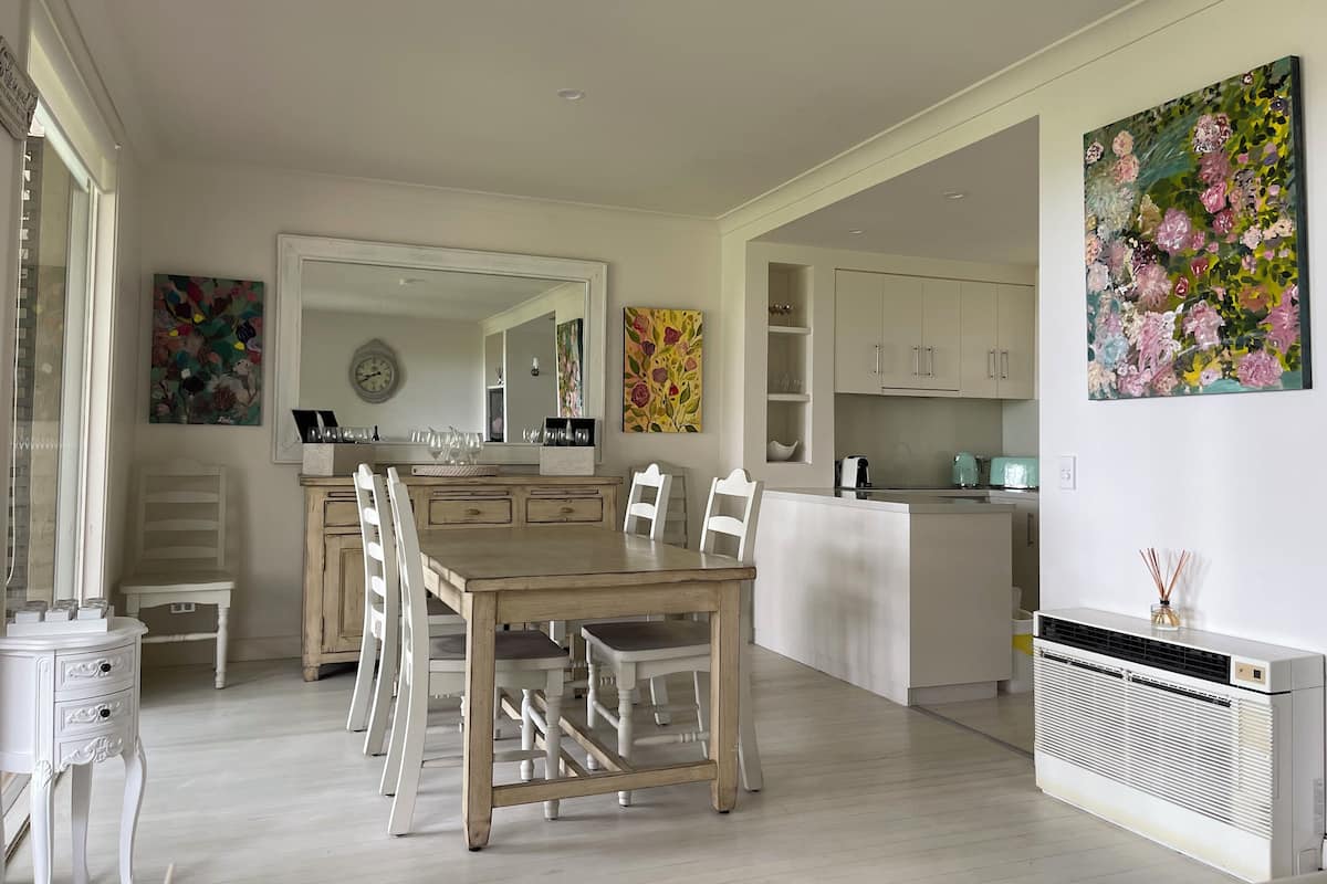 A modern kitchen with white cabinets, a large island, and a dining area with a wooden table and white chairs.