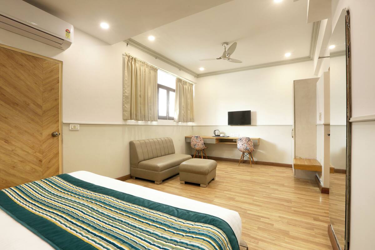 Una habitación de hotel con cama, sofá, reposapiés, escritorio con dos sillas, televisor y ventilador de techo.