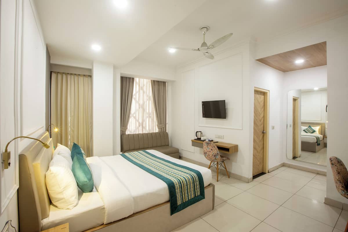 Habitación de hotel con cama, escritorio, silla, televisor y ventilador de techo.