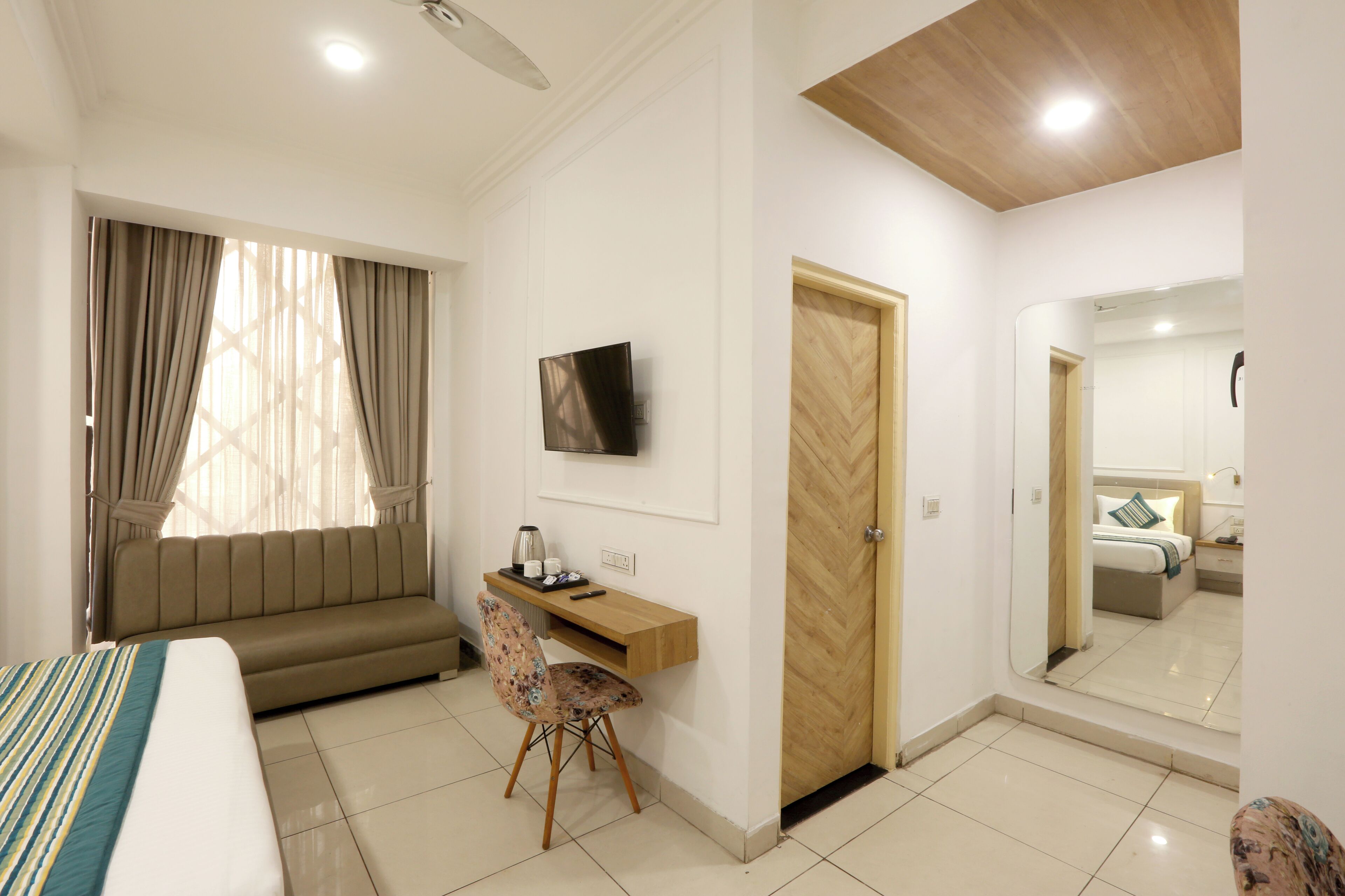 A hotel room with a bed, a desk with a chair, a television, and a large mirror.