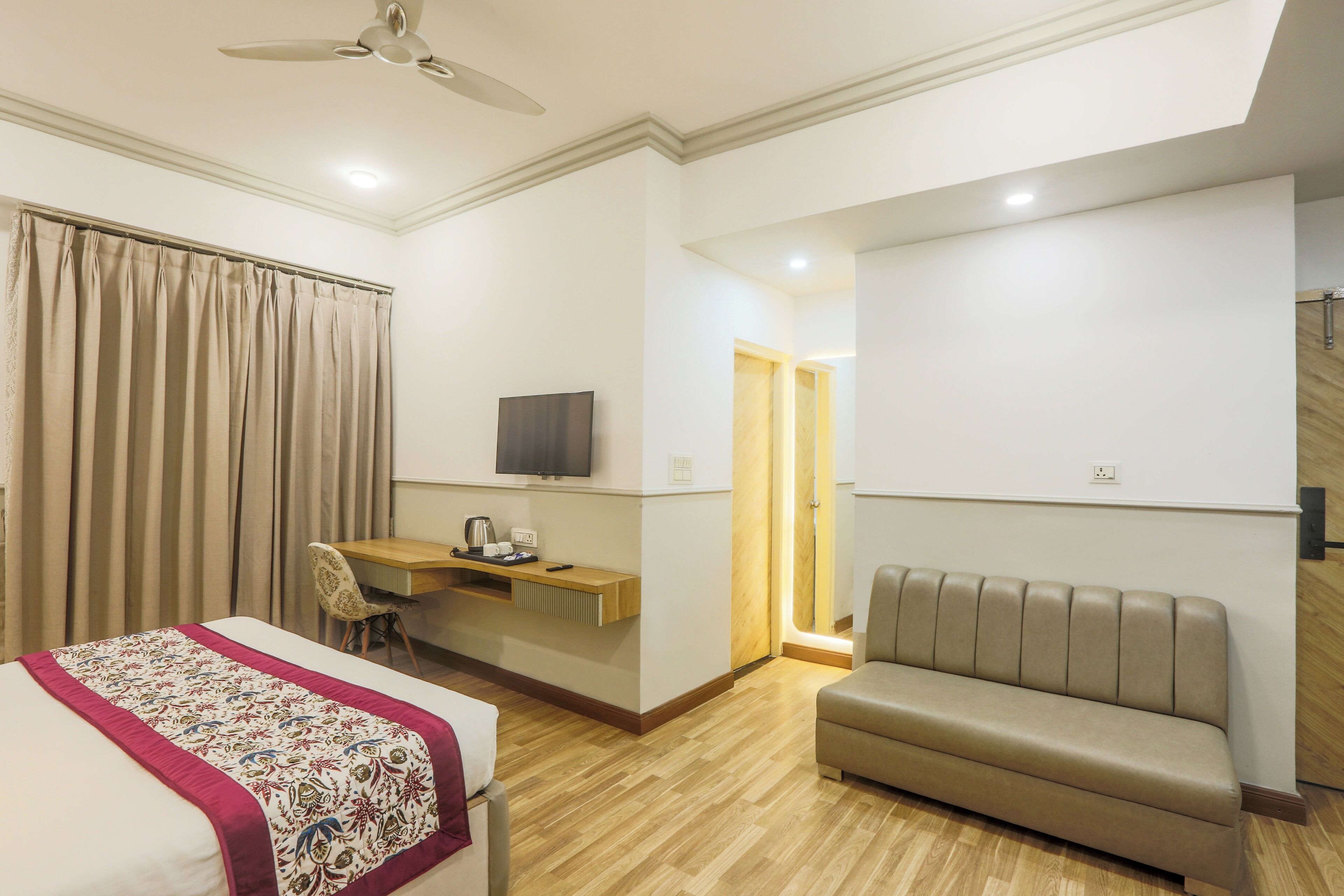 Habitación de hotel con cama, escritorio con silla, sofá y televisor en la pared.