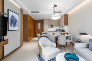 Ein modernes Hotelzimmer mit Essbereich, Flachbildfernseher, großem gerahmten Kunstwerk und minimalistischem Design.