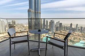 Ein Balkon mit Tisch und zwei Stühlen, mit Blick auf eine Skyline mit Hochhäusern und einem Gewässer.