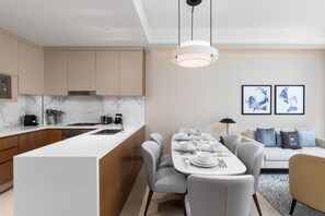 A modern kitchen with a central island, a dining area with a table set for four, and a living area with a sofa and two framed artworks.