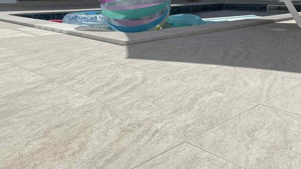 A large, colorful beach ball in a courtyard with a pool and white walls.