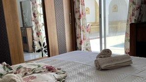 Een hotelkamer met een bed, bloemen gordijnen en uitzicht op een binnenplaats.