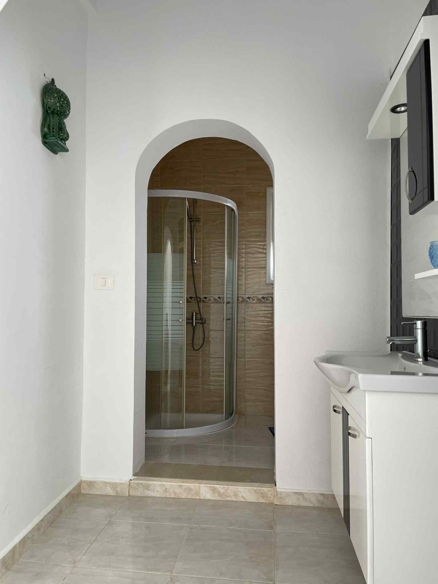 Une salle de bain moderne avec une douche à parois de verre, des meubles blancs et un sol carrelé.