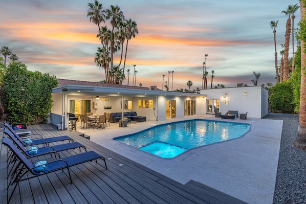 A modern house with a swimming pool, outdoor seating, and palm trees.