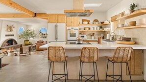 Uma cozinha espaçosa com vigas de madeira, uma ilha grande com banquetas e uma lareira.