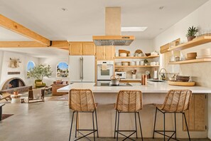 A spacious kitchen with wooden beams, a large island with bar stools, and a fireplace.