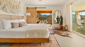 Um quarto espaçoso com uma cama grande, um ventilador de teto, vista para o exterior e decoração rústica.