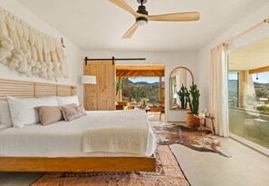 A spacious bedroom with a large bed, a ceiling fan, a view of the outdoors, and a rustic decor theme.