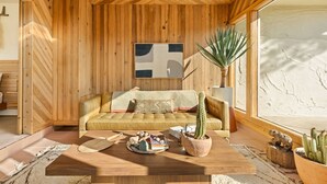 Uma sala de estar aconchegante com teto de madeira, um sofá com almofadas, uma mesa de centro com objetos decorativos e uma janela grande.