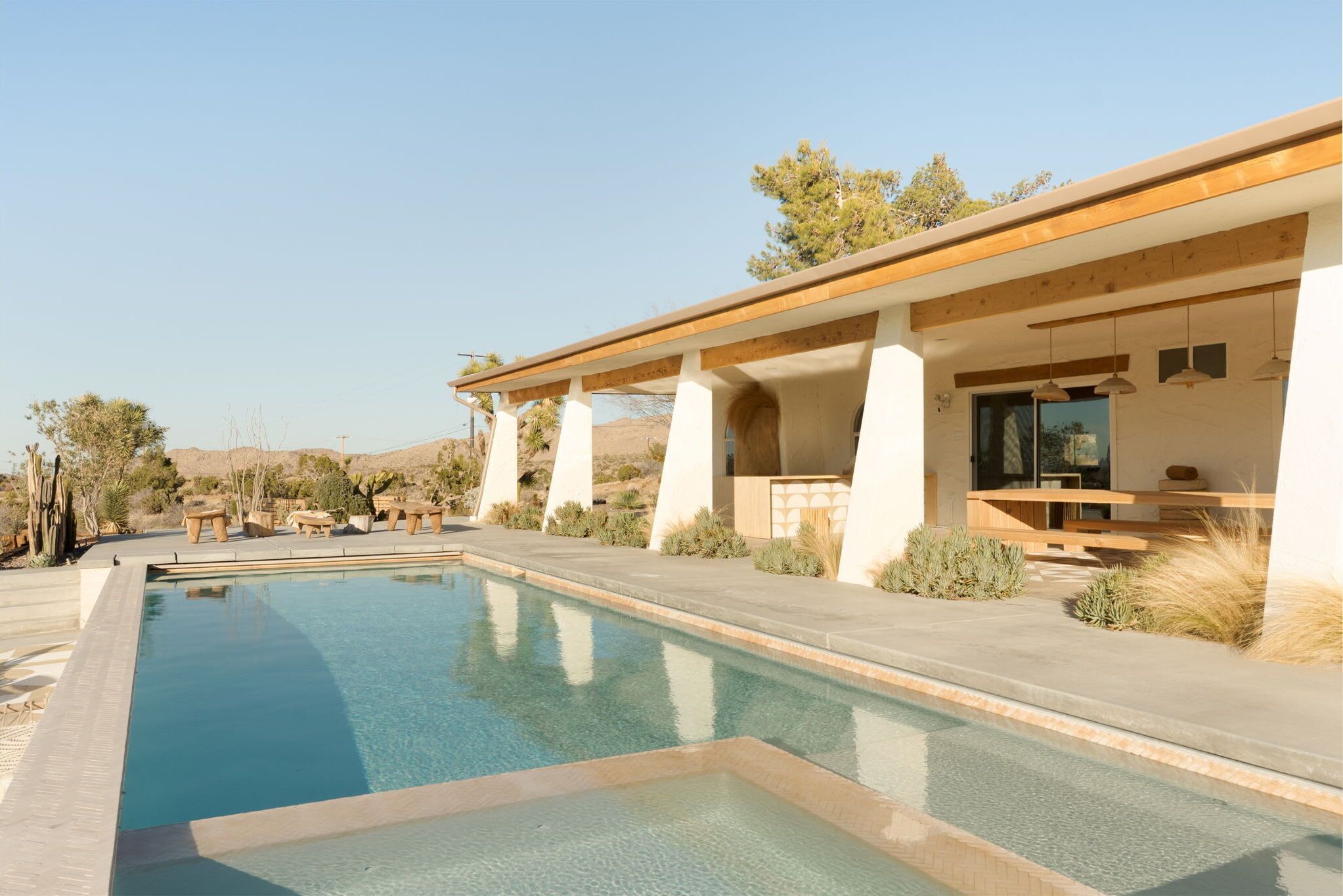 A modern pool area with clear blue water, surrounded by a patio with wooden beams and outdoor furniture.