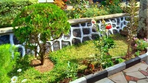 A building with a stone pathway leading to a door, surrounded by well-maintained gardens and a variety of plants. - Marangu Summit Lodge (Marangu)