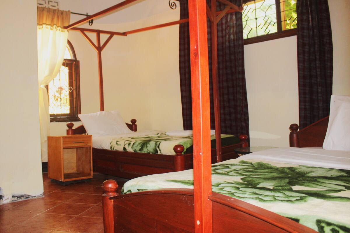A four-poster bed with a floral bedspread, a wooden nightstand, and a window with curtains.