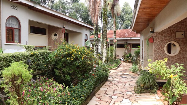 A courtyard with a stone pathway, lush greenery, and a building with a tiled roof and arched windows. - Marangu Summit Lodge (Marangu)