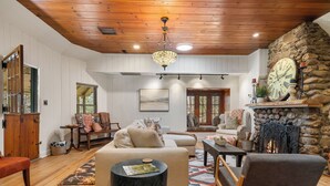 A cozy living room with a fireplace, wooden ceiling, and a stone wall. - Hottub/Arcade/Historic Cabin/Mins to AVL & WVL (Weaverville)