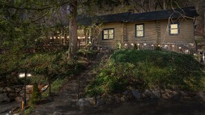 A log cabin with a stone staircase leading to the entrance, surrounded by dense foliage and a wooden deck. - Hottub/Arcade/Historic Cabin/Mins to AVL & WVL (Weaverville)