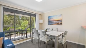 A dining area with a table and chairs, a view of greenery outside, and a painting on the wall.