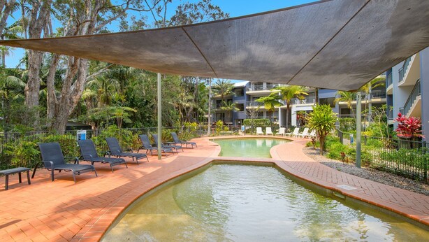 Un espace piscine avec des chaises longues, un élément décoratif aquatique et un bâtiment doté de balcons.