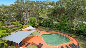 A swimming pool with a surrounding deck, sun loungers, and a large umbrella providing shade.
