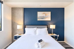 Una habitación de hotel con una cama grande, dos mesitas de noche con lámparas, un cuadro en la pared y una ventana.