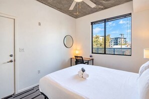A hotel room with a bed, a desk, a chair, a window with a view, and a ceiling fan.