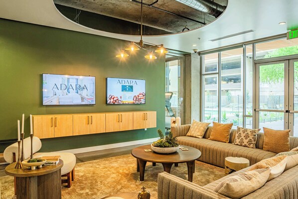 Un salon moderne avec un mur d’accent vert, un meuble en bois, un ensemble de canapés, une table basse et une grande fenêtre donnant sur l’extérieur.