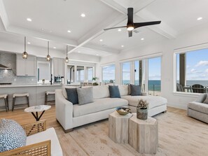 A modern living room with a large sofa, a coffee table, and a view of the ocean.
