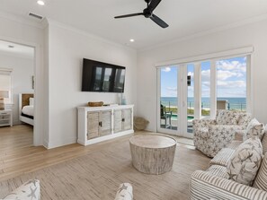 A spacious living room with a large TV, a ceiling fan, a round coffee table, and a sofa with star-patterned cushions.