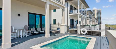 A rooftop pool area with a clear blue pool, outdoor seating, and a view of the ocean.