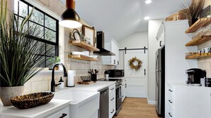 A modern kitchen with white cabinetry, a large window, and a wooden floor. - Little White House of Wimberley I River access (Wimberley)