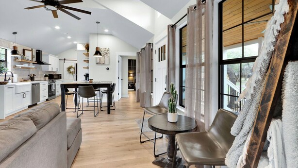 A modern kitchen with white cabinets, a dining area with a round table and chairs, and a ceiling fan. - Little White House of Wimberley I River access (Wimberley)