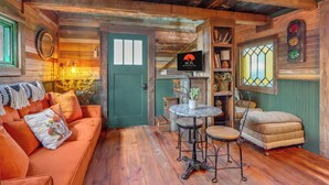 L’intérieur d’un chalet accueillant, avec un plancher en bois, une porte verte, un canapé avec des coussins, une petite table ronde et une chaise.