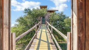 Un escalier en bois mène à un bâtiment dont la porte est verte, et qui est entouré d’arbres.