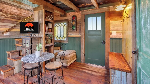 Un intérieur rustique en bois, avec une porte verte, une table ronde entourée de chaises et une enseigne ornée d’un logo représentant un cerf.