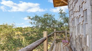 Une terrasse en bois avec un fauteuil rustique, un mur en bois orné d’un motif géométrique et un ciel dégagé.