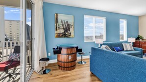 A room with a blue wall, a wooden barrel, a blue sofa, and a painting of a pier. - Ocean View l 5BR l Pool l Sleeps 16 l Luxury Villa (north myrtle beach)