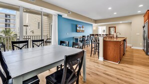 A modern kitchen with a wooden island, a dining area with chairs, and a view of the outside balcony. - Ocean View l 5BR l Pool l Sleeps 16 l Luxury Villa (north myrtle beach)