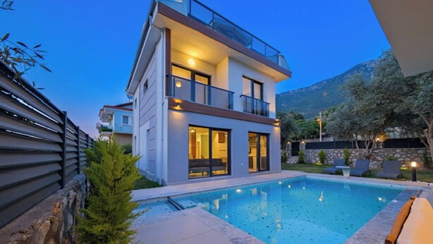 Une maison moderne à deux étages, dotée d’une piscine, de grandes fenêtres et d’un balcon.