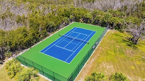 Vista aérea de una cancha de tenis rodeada de un bosque denso.